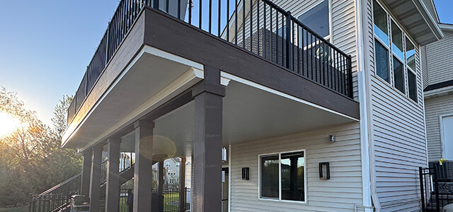 View of a two-story house with a raised deck with suspended-style underdecking installed, photographed from below at sunset.