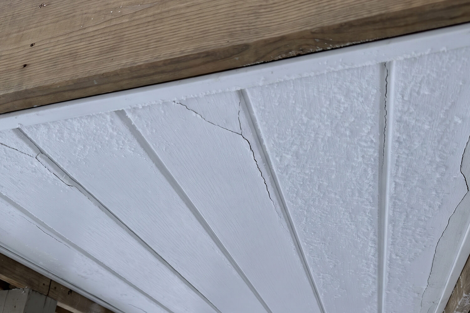 White painted wooden ceiling panels with visible cracking and peeling paint, bordered by unfinished wood beams.